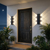 Two solar wall wash lights mounted vertically either side of dark timber front door at night creating warm symmetrical diamond light pattern with tropical plants