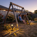 Solar garden path light casting warm star-like shadows on backyard lawn at twilight, with a child swinging nearby and native Australian plants in background — ideal for family-friendly outdoor spaces and safe evening play areas.