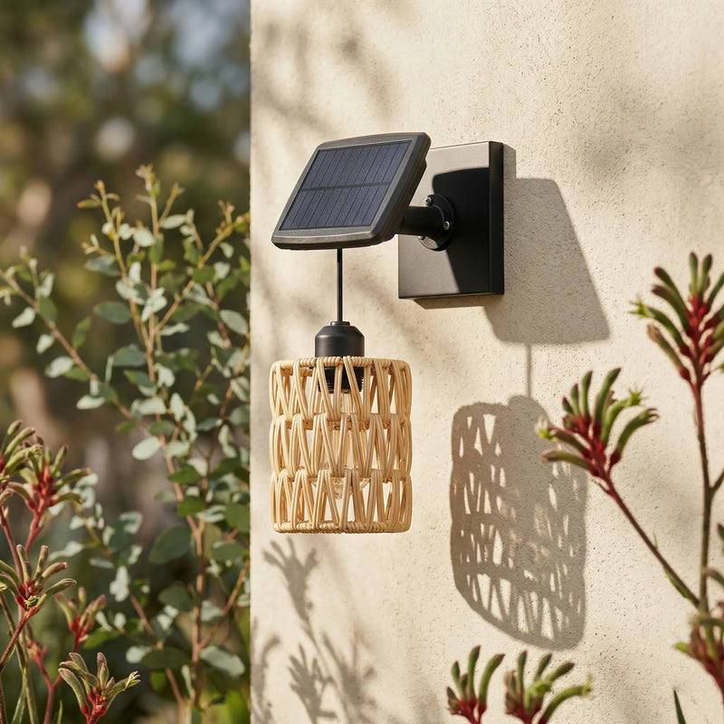 Kasa Solar Woven Wall Light mounted on an exterior cream wall, featuring a handwoven PE rattan shade and adjustable monocrystalline solar panel, surrounded by native Australian plants. Highlights its weatherproof design and seamless integration into natural garden settings.