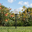 A crystal-textured globe solar path light on a black stake installed in a sunny green garden.