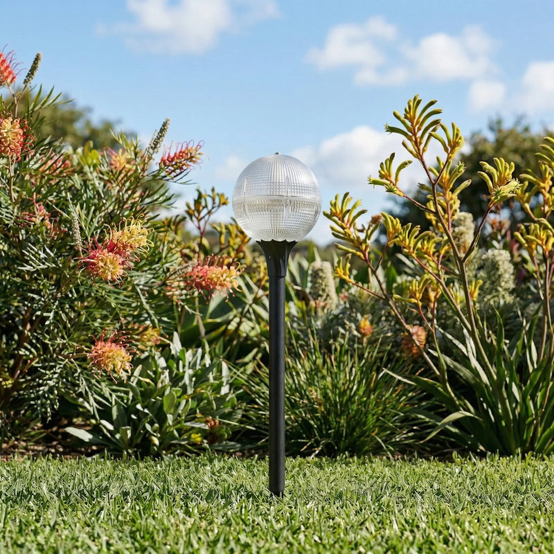 A crystal-textured globe solar path light on a black stake installed in a sunny green garden.