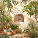 PT0907 Solar Woven Hanging Pendant Light hanging in a sunlit garden courtyard with potted plants and stone walls, showcasing its handwoven PE rattan shade and natural boho aesthetic for outdoor decor.