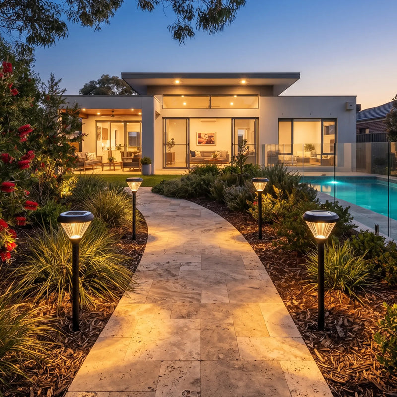 Solar lawn lights illuminate a stone path beside a pool at dusk, casting warm glow on modern home and garden beds.