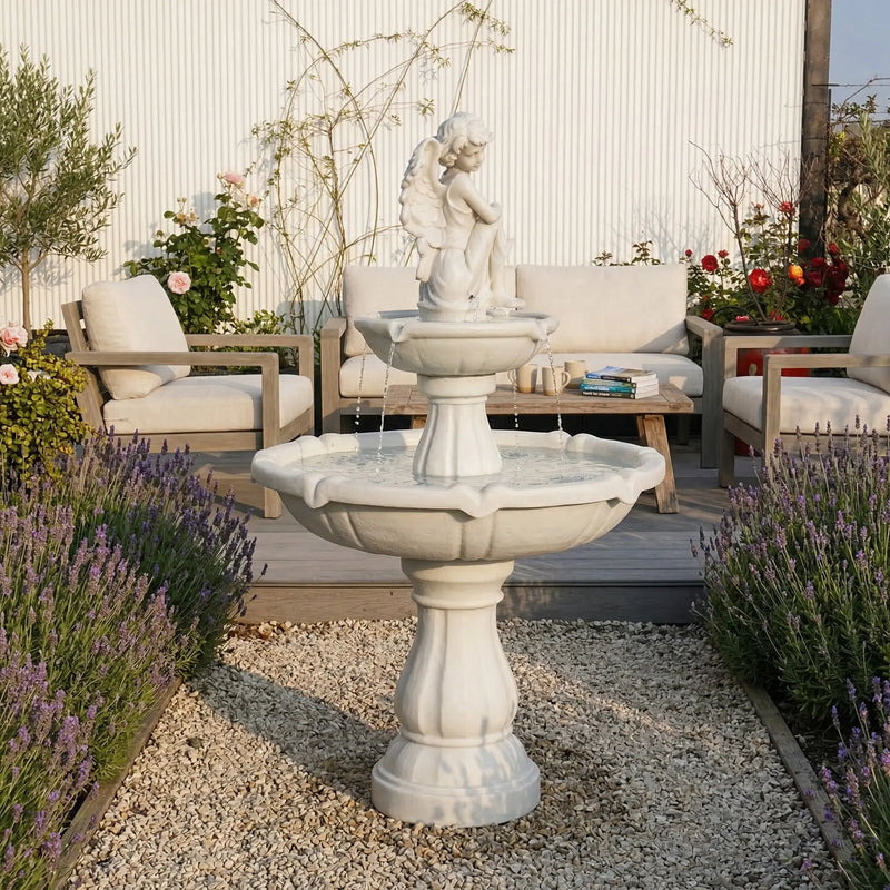 OUTWAY angel solar garden fountain with winged angel figure on top tier displayed on a gravel courtyard surrounded by lavender and roses with outdoor timber lounge furniture and coffee cups in the background