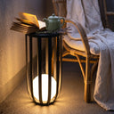 Decorative table with a glowing light base, book, teapot, and lavender near a wicker chair.