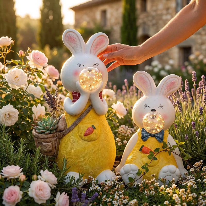 OUTWAY Hoppi A004 solar bubble rabbit garden ornament pair in a Tuscan-style rose and lavender garden at golden hour with a hand placing the standing rabbit holding succulents in a basket