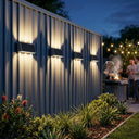 Outdoor setting with people around a grill, illuminated by wall-mounted lights on a metal fence.