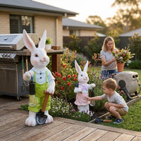 Lumi A002 boy and girl rabbit solar garden ornaments placed on a backyard deck beside a BBQ grill while a mother arranges flowers and a young boy touches the girl rabbit in an Australian garden at golden hour