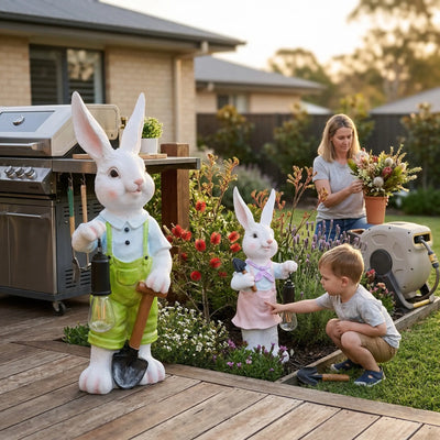 Lumi A002 boy and girl rabbit solar garden ornaments placed on a backyard deck beside a BBQ grill while a mother arranges flowers and a young boy touches the girl rabbit in an Australian garden at golden hour