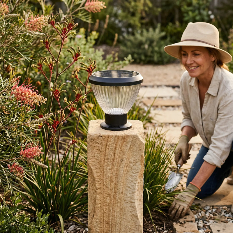 OUTWAY Priva PT0111 solar pillar cap light on a sandstone post in an Australian native garden with kangaroo paw flowers while a woman in a hat gardens along a gravel pathway