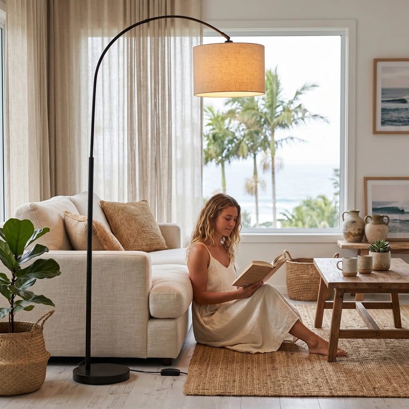Woman reading a book in a cozy living room with a large window, floor lamp, and decorative items.