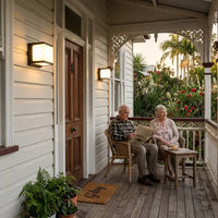 Elderly couple relaxing on a heritage Queensland home verandah at dusk, with two Outawy solar wall lights glowing warmly beside the front door.