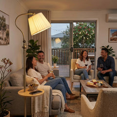 FL068 antique brass floor lamp with round wood tray beside a grey linen sofa, glowing warm amber, four friends enjoying wine in a cozy Australian living room at night