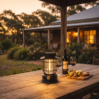 Vintage solar lantern on wooden table with wine and cheese, glowing warmly at dusk in a rustic backyard setting.