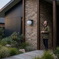 Man standing outside a modern house with a light fixture on the wall.