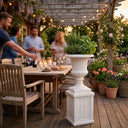 Outway F005 F006 Petra roman sandstone planter pedestal on timber deck beside outdoor dining table string lights dusk herbs