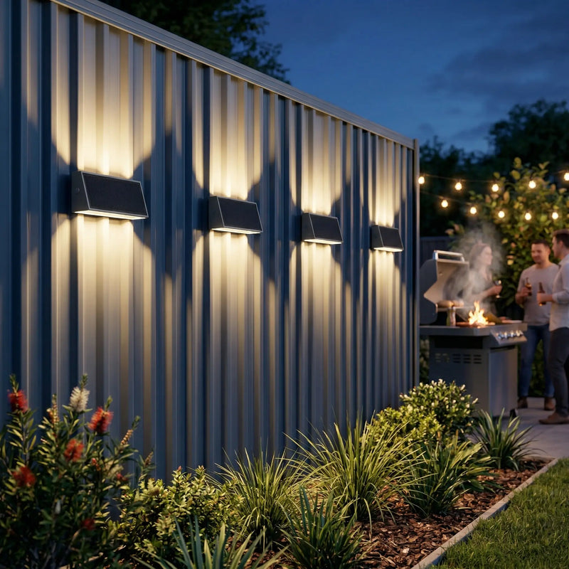Tenox PT0716 solar wall lights mounted on grey Colorbond fence, casting warm up-and-down glow at dusk, Australian backyard BBQ setting