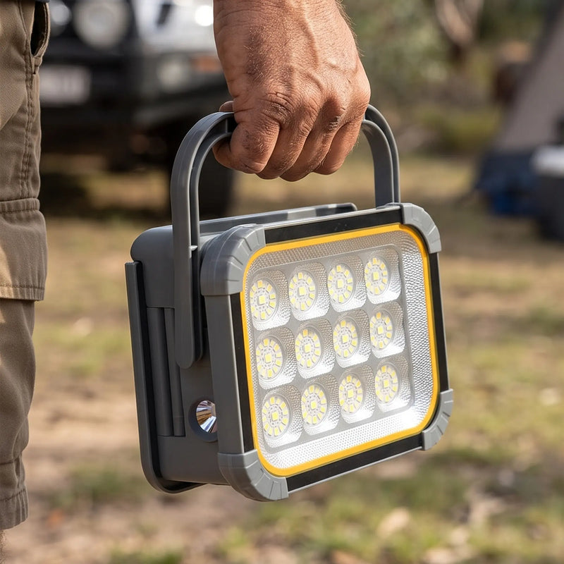 Hand holds SolarFlex Pro flood light; 12 LEDs, yellow trim, grey rugged casing for outdoor camping use.
