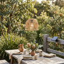 Outdoor dining table setting with a wicker pendant light and natural decor in a garden.