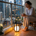 Woman sitting on a balcony at night holding a mug, with city lights in the background.