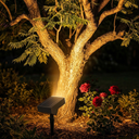 Solar-powered outdoor light illuminating a tree and flowers in a garden at night.