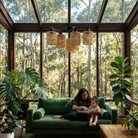 Woman and child reading on a green couch in a room with large windows and plants.
