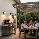 Three Serra solar wall lights illuminating outdoor BBQ entertaining area with family and friends dining under pergola at dusk