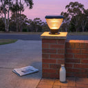 OUTWAY Priva PT0111 solar pillar cap light glowing warm white on a brick gate pillar at dusk in an Australian suburban driveway with a newspaper and milk bottle on the ground