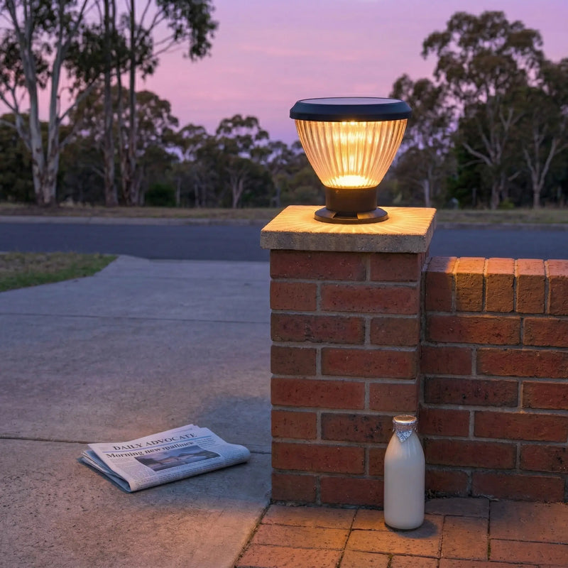 OUTWAY Priva PT0111 solar pillar cap light glowing warm white on a brick gate pillar at dusk in an Australian suburban driveway with a newspaper and milk bottle on the ground