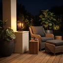 HeritagePost Solar Column Light placed on brick pillar beside wicker armchair on wooden deck at night, highlighting its use as ambient patio lighting that complements outdoor lounging areas with tropical plants and cozy decor.