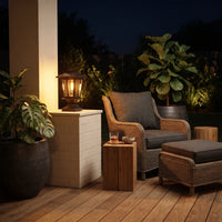 HeritagePost Solar Column Light placed on brick pillar beside wicker armchair on wooden deck at night, highlighting its use as ambient patio lighting that complements outdoor lounging areas with tropical plants and cozy decor.