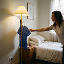 Person reaching for a blue shirt on a coat rack in a bedroom.