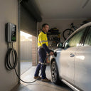 A man in workwear charging a silver SUV with an Outway wallbox charger in a home garage.