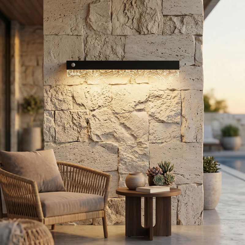Outdoor setting with a stone wall, wicker chair, and table with plants, illuminated by a modern wall light fixture.