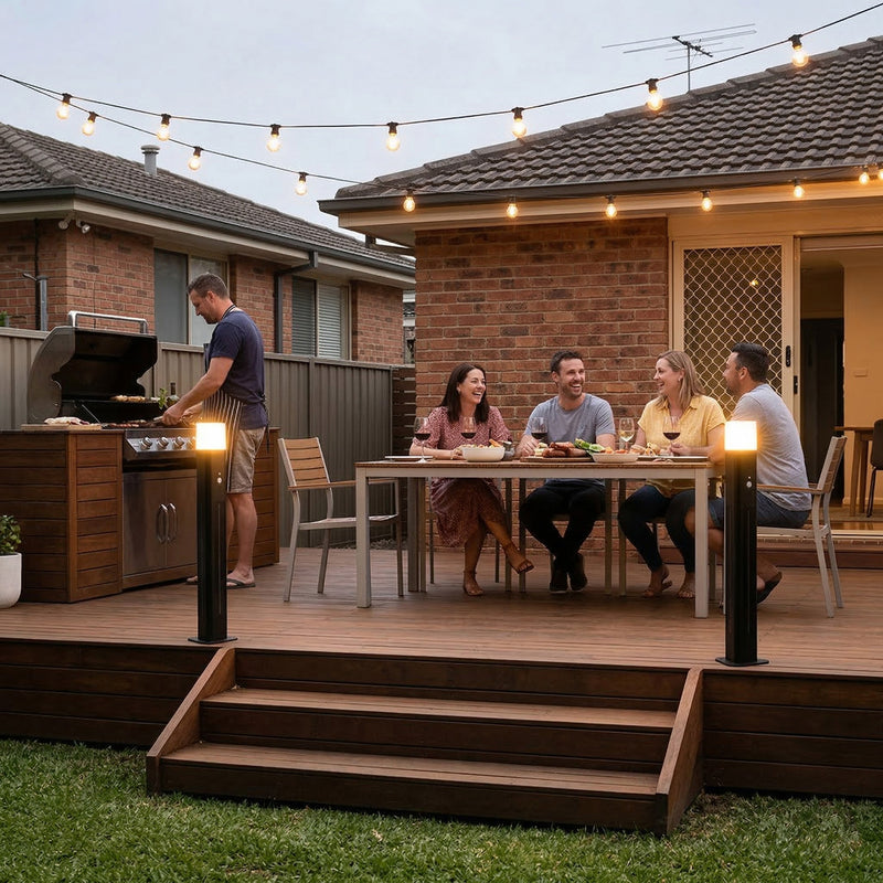 People sitting around a table on a backyard deck with string lights and a barbecue.