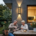 Man pouring wine for a woman at a table outside a modern house.