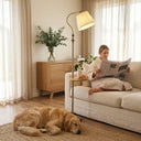 FL068 antique brass arc floor lamp with wood tray next to a cream sofa, warm white light, woman in bathrobe reading a newspaper with a golden retriever resting nearby