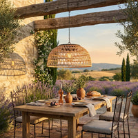 Outdoor dining setup with a wooden table, chairs, and a wicker pendant light in a scenic setting.