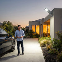 Man standing on a modern residential driveway lit by the OUTWAY Nexa T007 solar security light mounted on the garage wall.