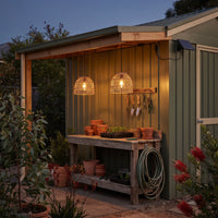 Two PT0914 lanterns illuminating potting shed workspace at twilight, solar panel mounted on roof edge — practical lighting for gardening tasks with rustic charm.