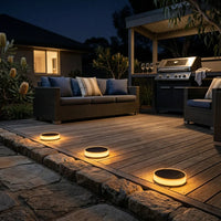 Alt Text: Warm white solar deck lights installed on wooden decking at night, illuminating an outdoor patio and BBQ area, creating a cozy backyard ambiance.