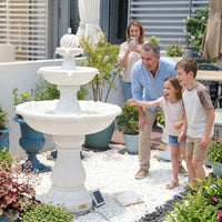 Family of four by a two-tiered white fountain on a patio with plants and furniture.