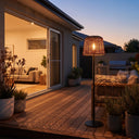 Solar floor lamp glowing on timber deck at dusk — complements sliding glass door and outdoor sofa, creating resort-style ambiance with handwoven PE rattan shade and anti-rust iron frame.