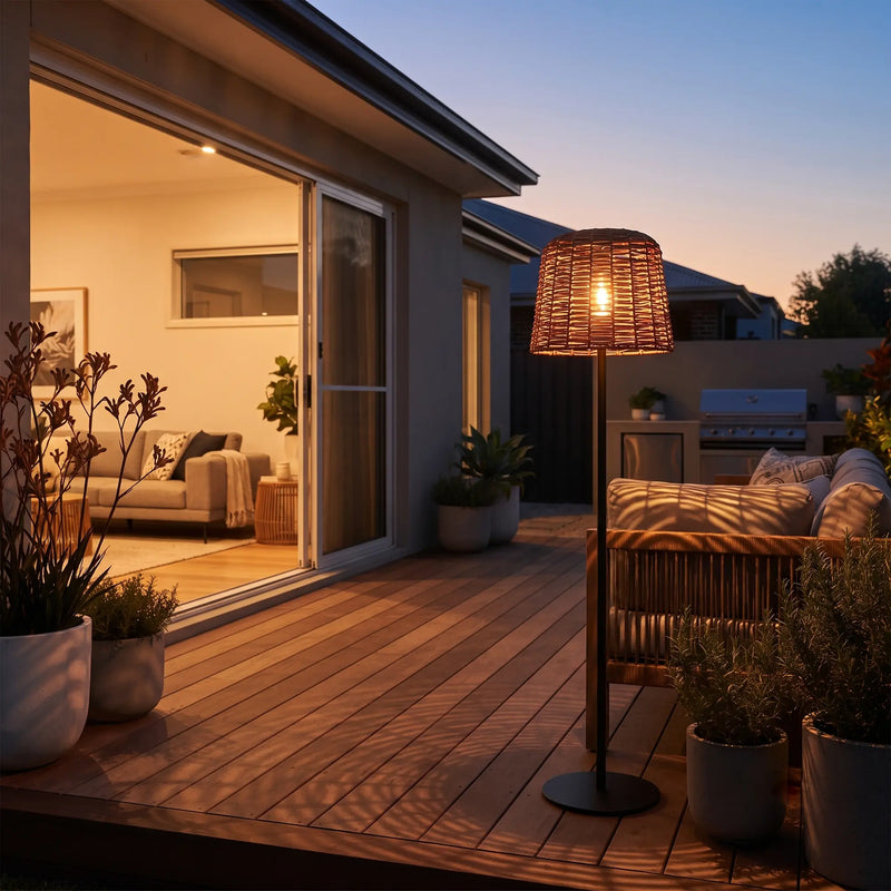 Solar floor lamp glowing on timber deck at dusk — complements sliding glass door and outdoor sofa, creating resort-style ambiance with handwoven PE rattan shade and anti-rust iron frame.