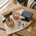 Solar-powered outdoor light set with rattan shades, remote control, and packaging on a wooden surface.