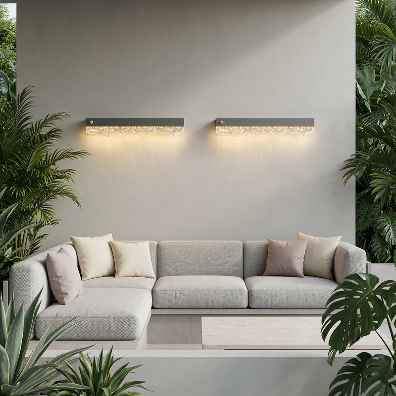 Gray sectional sofa with decorative pillows in a modern outdoor setting with wall lights and plants.