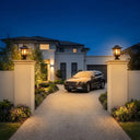 Two HeritagePost Solar Lanterns flanking driveway entrance to luxury home with parked SUV, showcasing their role as symmetrical gateway lighting that elevates architectural presence and guides vehicles with warm, consistent illumination.