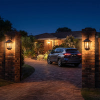 Two HeritageGlow Solar Lanterns mounted on brick pillars framing driveway entrance to suburban home with parked SUV, showcasing their role as symmetrical gateway lighting that elevates architectural presence and guides vehicles with warm, consistent glow.