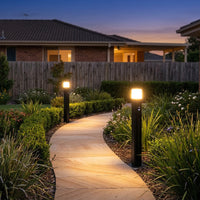Two PT0730 Virgo solar bollard lights casting warm 3000K glow along winding garden path with lush green landscaping and Australian brick home at twilight