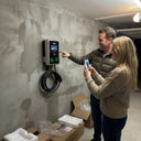 A couple setting up the Outway EV04 smart charger, using a smartphone app to control the wall-mounted unit